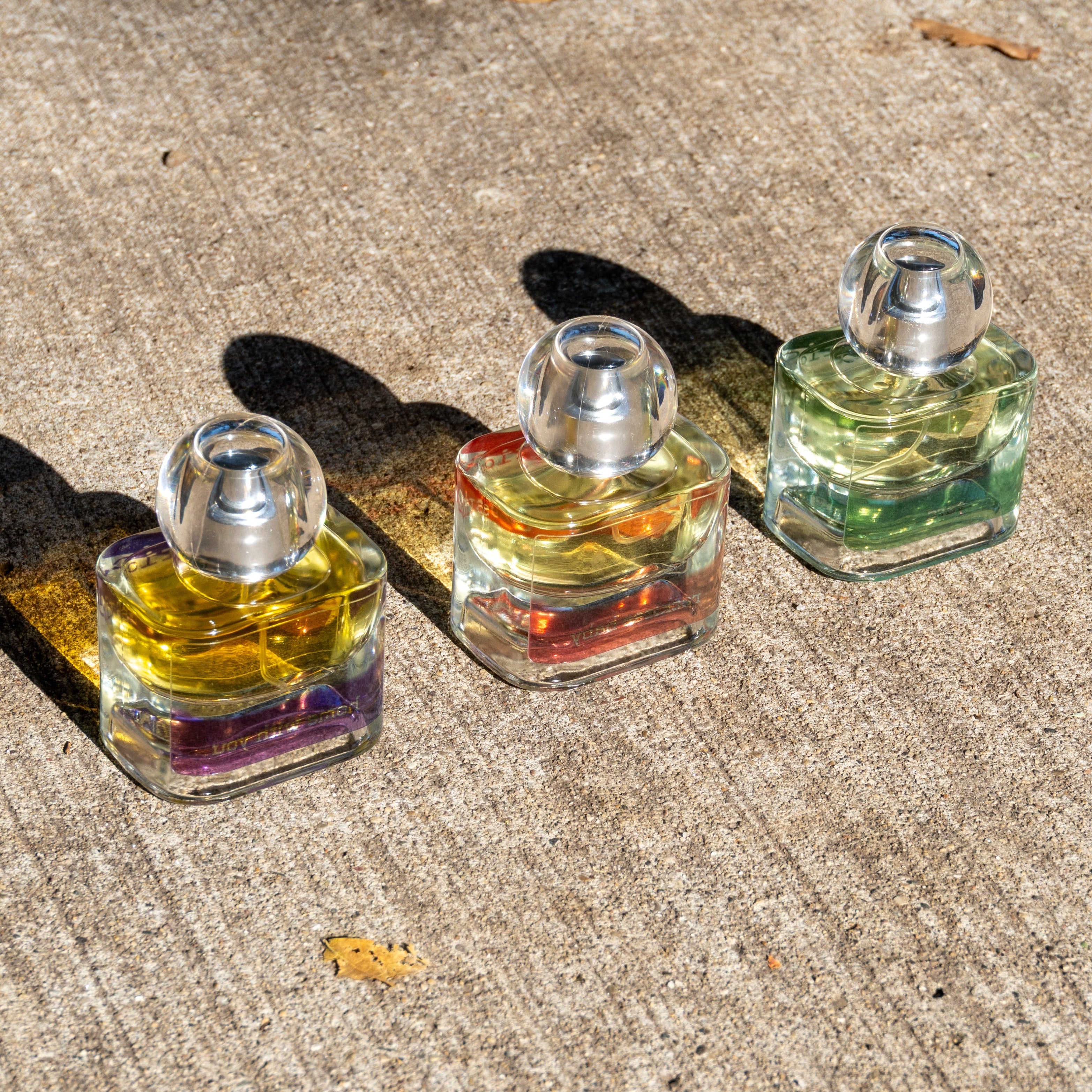 Three small perfume bottles with different colored liquids on a concrete surface.