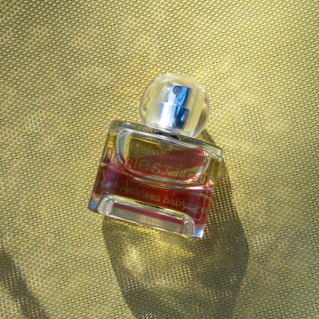 Perfume bottle labeled 'Domestica' and 'Reckless baby' on a textured gold surface.