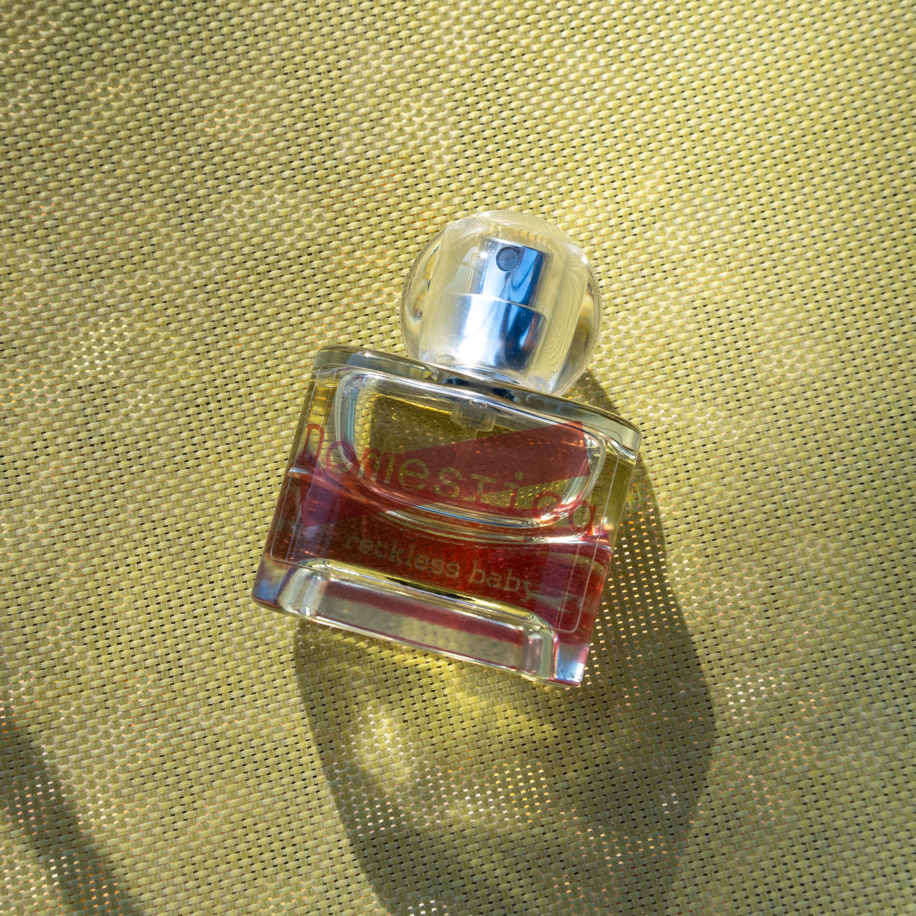 Perfume bottle labeled 'Domestica' and 'Reckless baby' on a textured gold surface.