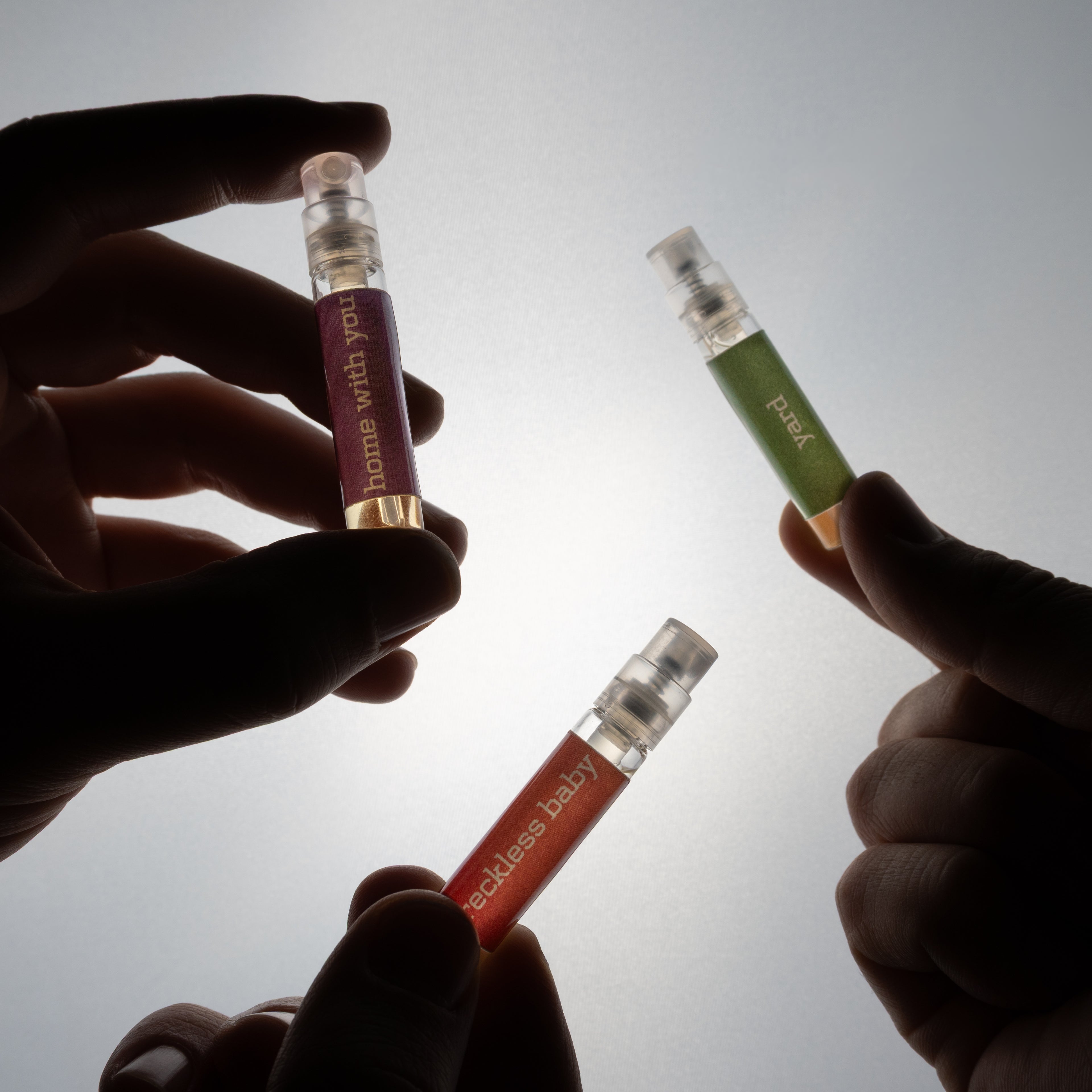 Three small bottles held by hands against a light background